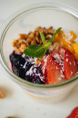 Sağlıklı diyet kahvaltı. Beyaz arka planda cam bir kavanozda Chia tohumlu, meyveli ve fındıklı yulaf ezmesi.