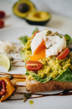 Ezilmiş avokadoyla sandviç ve beyaz tabakta domatesli haşlanmış yumurta.
