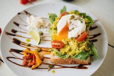 Ezilmiş avokadoyla sandviç ve beyaz tabakta domatesli haşlanmış yumurta.