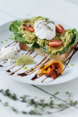 Ezilmiş avokadoyla sandviç ve beyaz tabakta domatesli haşlanmış yumurta.