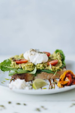 Ezilmiş avokadoyla sandviç ve beyaz tabakta domatesli haşlanmış yumurta.