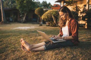 Laptoplu genç bir kadın yeşil çimlerde oturuyor.