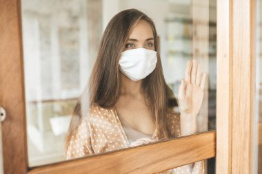 Tıbbi maskeli genç bir kadın kendini karantinaya almak için evde karantinada kalıyor. Ev karantinası, COVID-19 önleme, Coronavirüs salgını durumu