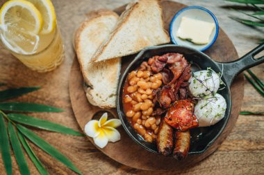İki yumurtalı kahvaltı, sosis, pastırma, fasulye ve ahşap masada limonata. Yukarıdan görüntüle