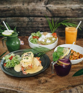 Kafede akşam yemeği, yumurtalı Benedict, avokado ile tost, karidesli makarna ve ahşap arka planda içecekler.