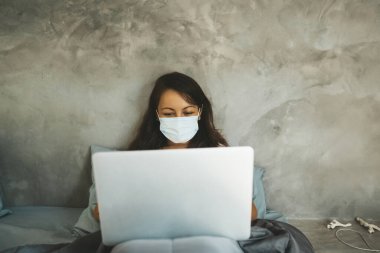 Maskeli kadın dizüstü bilgisayarla yatakta yatıyor. Boşluğu kopyala.