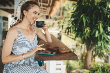 Sarışın kadın bir kafede kahve içiyor, akıllı telefon kullanıyor.