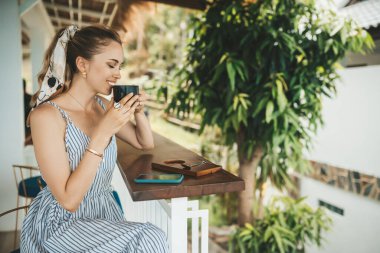 Sarışın kadın bir kafede kahve içiyor, akıllı telefon kullanıyor.