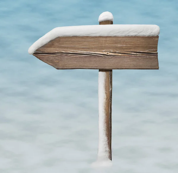Wooden direction sign with less snow on it on snow background
