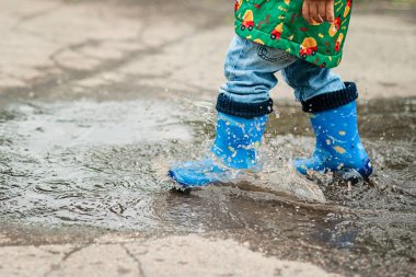 Su birikintisine oynarken küçük çocuk yağmurluk ve lastik çizmeler