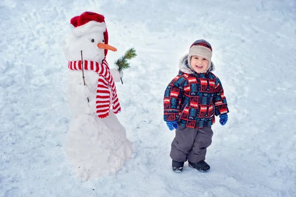 Happy beautiful child building snowman in garden, winter time, — Stock Photo, Image