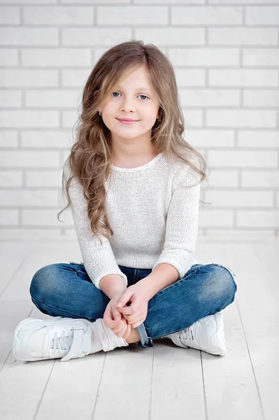 Portrét roztomilá malá 7 let stará dívka usmívá a sedí na bílém dřevěnou podlahu ve studiu — Stock fotografie