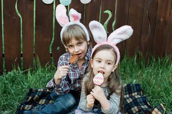 Little girl and boy eat a gingerbread cookie in the shape of the Easter egg. — Stock Photo, Image