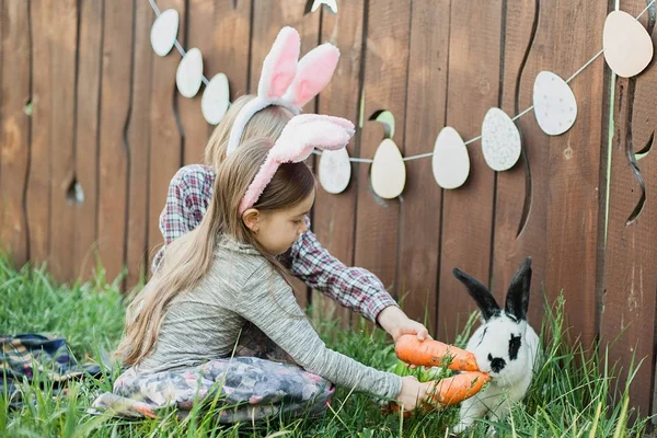 Zabaw się z prawdziwym króliczym. Śmiejąc się dziecko na Easter egg hunt z biały króliczek pieścić. Mała dziewczynka maluch bawi się zwierzęcego w ogrodzie. Chłopiec karmienia królik marchew. — Zdjęcie stockowe