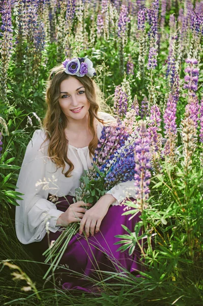 Belle jeune fille en robe ultra violette et blanche tenant un bouquet de lupin au coucher du soleil sur le terrain. Le concept de nature et de romantisme. Le tonifiant — Photo