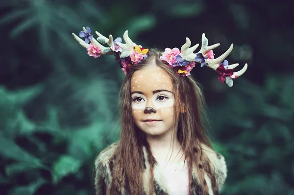 Märchenhafte Mädchen. Porträt eines kleinen Mädchens im Hirschkleid mit gemaltem Gesicht im Wald. großes braunes Geweih — Stockfoto
