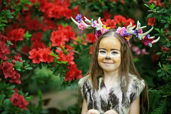 Chica de cuento de hadas. Retrato de una niña pequeña en un vestido de ciervo con una cara pintada en el bosque. Cuerno marrón grande —  Fotos de Stock