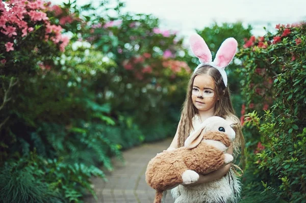 Children play with toy rabbit. Laughing child at Easter egg hunt with pet bunny. Little toddler girl playing with animal in the garden.