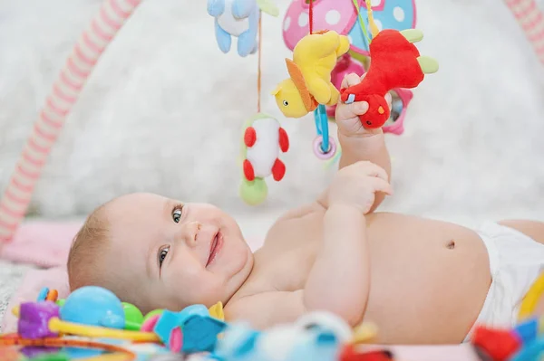 Baby lying on Developing rug. playing in Mobile. educational toys. Sweet child Crawling And Playing With Toys On Carpet Stock Photo