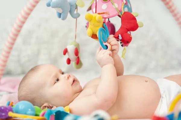 Bebê deitado no tapete em desenvolvimento. tocando em Mobile. brinquedos educativos. Doce criança rastejando e brincando com brinquedos no tapete — Fotografia de Stock