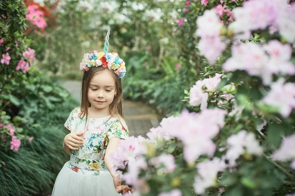 Fantasy little girl with rainbow unicorn horn with flowers in azalea park — Stock Photo, Image