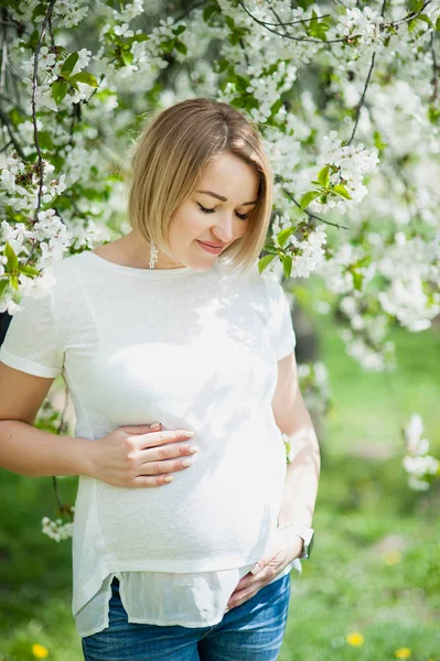 Весняний настрій, красива вагітна жінка пахне квітучим вишневим деревом, насолоджуючись природою, білим квітковим садом . — стокове фото