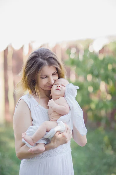 Güzel bir genç anne kucağında bir bebekle bahçede duran. — Stok fotoğraf