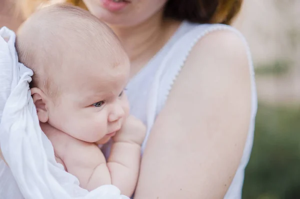Egy gyönyörű fiatal anya a csecsemőt a karjaiban áll a kertben. — Stock Fotó