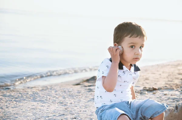 可爱的小男孩听海贝壳在海滩上的声音 暑期度假理念 — 图库照片