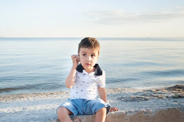 可爱的小男孩听海贝壳在海滩上的声音 暑期度假理念 — 图库照片