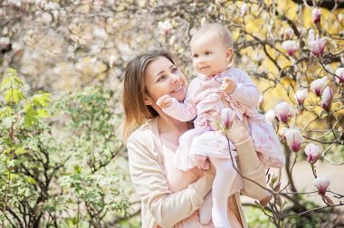 Güzel bir genç anne kucağında bir bebekle bahçede duran.