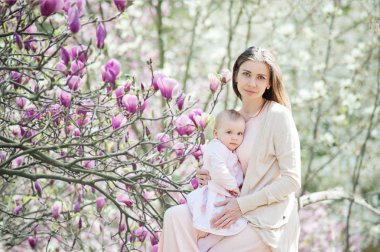 Güzel bir genç anne kucağında bir bebekle bahçede duran.