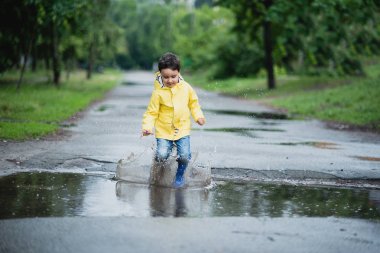 Su birikintisine oynarken küçük çocuk yağmurluk ve lastik çizmeler