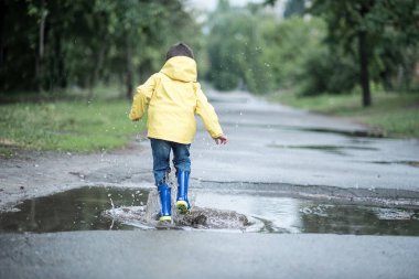 Islak bir çocuk bir su birikintisine, arkadan görünüm atlıyor