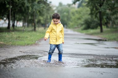 Islak bir çocuk bir su birikintisine atlıyor. Eğlenceli sokak. 