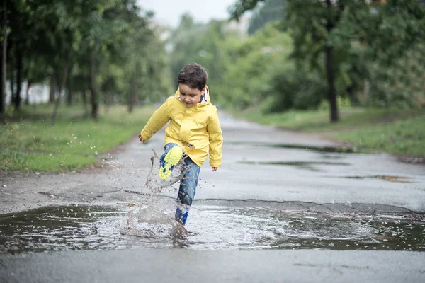 Islak bir çocuk bir su birikintisine atlıyor. Eğlenceli sokak. 