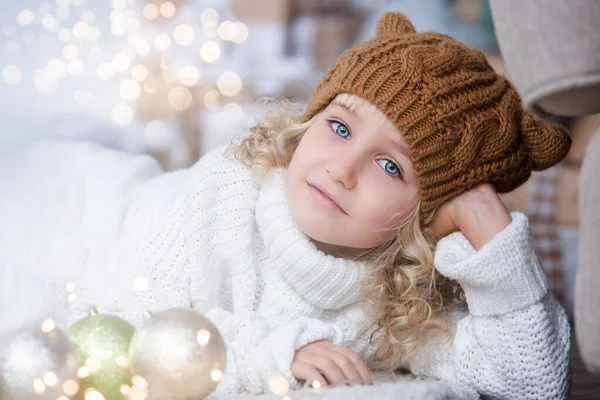 Menina em chapéu de malha perto da árvore de Natal faz um desejo de ano novo . — Fotografia de Stock