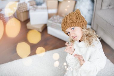 Noel ağacının yanında örülmüş şapkalı bir kız yeni yıl dileği diliyor..