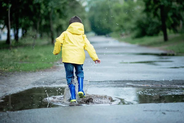 Islak bir çocuk su birikintisine atlıyor. Sokakta eğlenmek. Yazın sinirli. — Stok fotoğraf