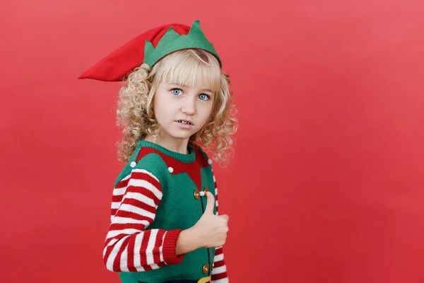 Niña en traje de ayudante de Santa elfo sobre fondo de color vivo rojo brillante . — Foto de Stock