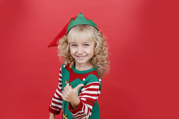 Niña en traje de ayudante de Santa elfo sobre fondo de color vivo rojo brillante . — Foto de Stock