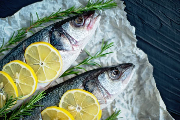 Two Raw fish fillet with spices, herbs, lemon and salt on black stone background