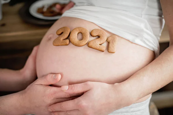 Foto cortada de mulher grávida segurando número 2020 de biscoitos de gengibre na barriga . — Fotografia de Stock