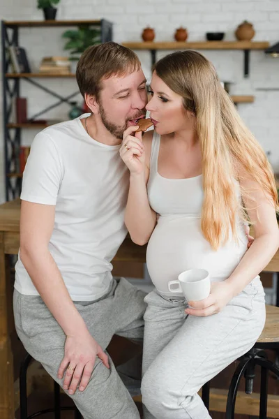 Έγκυος γυναίκα και ο σύζυγος Έχοντας πρωινό στην κουζίνα πίνουν καφέ ή φρέσκο χυμό και φιλιά. — Φωτογραφία Αρχείου