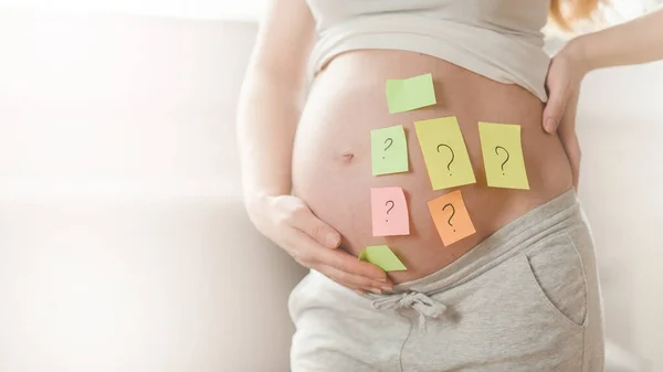 Έννοια της επιλογής του ονόματος του μωρού. κομμένο πλάνο της εγκύου γυναίκας με ερωτηματικά σε αυτοκόλλητα χαρτί στην κοιλιά, — Φωτογραφία Αρχείου