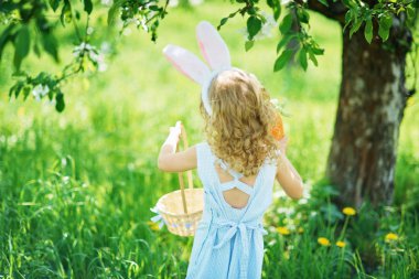 Paskalya tavşanı kulaklı sevimli kız bahçede sepetle yürüyor. Paskalya yumurtası avı konsepti 