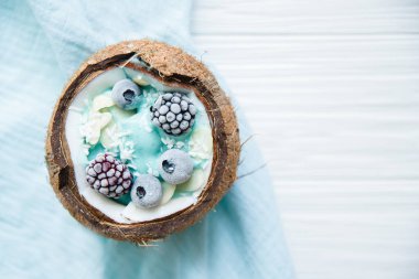 Üzerinde yabanmersini ve böğürtlenli chia tohumu olan muzlu hindistan cevizi kasesinden oluşan sağlıklı bir kahvaltı. vegan çiğ gıda konsepti