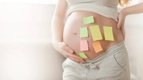 Έννοια της επιλογής του ονόματος του μωρού. κομμένο πλάνο της εγκύου γυναίκας με ερωτηματικά σε αυτοκόλλητα χαρτί στην κοιλιά, — Φωτογραφία Αρχείου