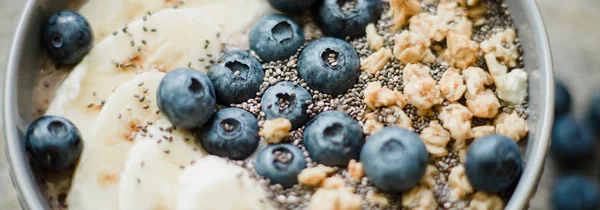 Healthy breakfast berry smoothie bowl topped with banana, granola, Blueberries and chia seeds with copy space