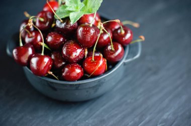 Koyu kayalıklardaki kasede su damlası olan taze kirazlar..